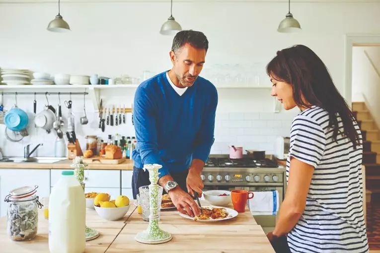 Man and woman cooking and eating in kitchen